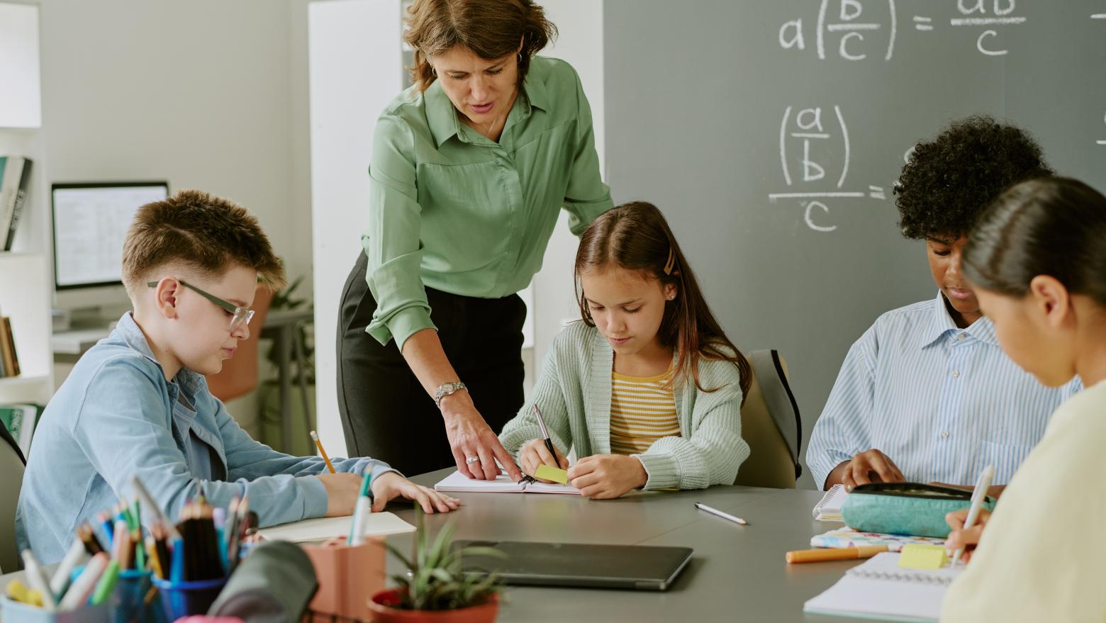 Eine Lehrerin kommt zu Schülern in einer Klasse an einen Tisch